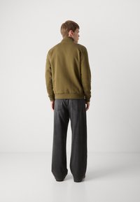 Olive spalvos užtrauktuku užsegama striukė su aukštu apykakle, gumuotomis rankogaliais ir apačia. Dėvima su laisvai krentantis tamsiai pilkais džinsais, turinčiais galinius kišenes.