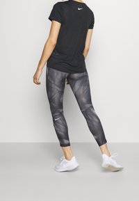 Svart atletisk tröja med korta ärmar och rund hals, kombinerad med grå leggings med ett geometriskt mönster och en vit Nike-logotyp. Vita sneakers.