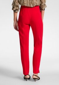 Pantaloni rossi su misura in un tessuto liscio, con vita alta e design attillato. Fessure notevoli alle caviglie esaltano la silhouette complessiva.