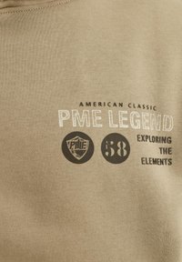Beige Sweatshirt mit bedrucktem Text: "AMERICAN CLASSIC PME LEGEND 58 EXPLORING THE ELEMENTS." Beinhaltet ein rundes schwarzes Logo.
