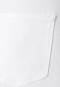 Tela de mezclilla blanca con un único bolsillo trasero y costuras visibles. Superficie texturizada con un diseño limpio y minimalista.