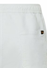 Witte broek met elastische tailleband en een achterzak met een klein zwart-geel merkembleem aan de rechterkant.