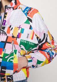 Kolorowa kurtka zapinana na zamek, z mieszanką geometrycznych wzorów i logo. Wykonana z lekkiego materiału, z elastycznymi mankietami i krawędzią.
