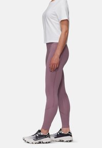 Lyse lilla leggings med en glat overflade og syningdetaljer, parret med en hvid kortærmet top og mønstrede løbesko.