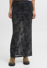 Gonna lunga nera con sovrapposizione in pizzo floreale, vita aderente, design trasparente, texture morbida e leggero svasamento all'orlo. Stivali marroni con tacco grosso.