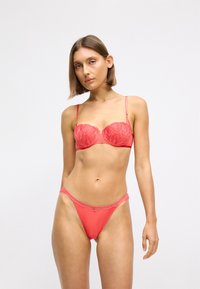 Σετ εσώρουχων σε κοραλί απόχρωση που περιλαμβάνει σουτιέν με ενισχύσεις και λεπτομέρειες από δαντέλα, συνδυασμένο με σλιπ χαμηλής μέσης με περίγραμμα από δαντέλα.