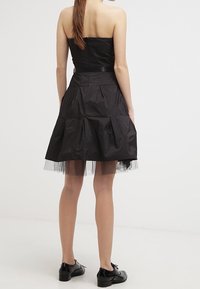Robe noire sans bretelles avec un corsage ajusté et une jupe évasée à plusieurs couches ornée d'accents en tulle. Stylisée avec des chaussures montantes noires à lacets.