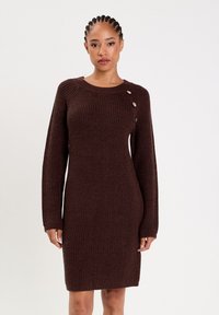Brown knitted dress with long sleeves, a ribbed texture, and a round neckline. Features decorative buttons on the left shoulder.