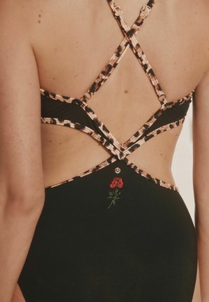 Rückansicht eines schwarzen Badeanzugs mit gekreuzten Leopardenmuster-Trägern und einer kleinen roten bestickten Rose im unteren Rückenbereich.