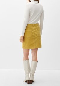 Gul kordancerad minikjol med bakfickor, kombinerad med en vit långärmad polotröja och knähöga vita klackstövlar.