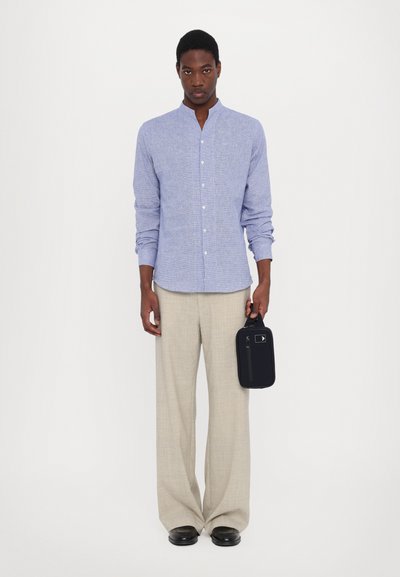Camicia azzurra a maniche lunghe con colletto a polo, pantaloni beige a gamba larga e una borsa nera con cerniera e manico.