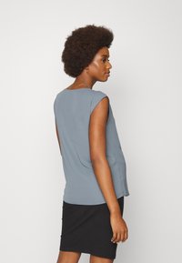 Top cinza sem mangas feito de tecido leve, com decote redondo e um corte solto. Combinado com uma saia preta canelada.