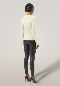Weißes, geripptes Langarmoberteil kombiniert mit schwarzen, kunstledernen Leggings und schwarzen High Heels. Glatte Texturen und figurbetontes Design.