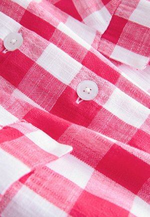 Tissu à carreaux rouges et blancs avec deux boutons blancs cousus dessus, montrant la texture détaillée et les coutures.