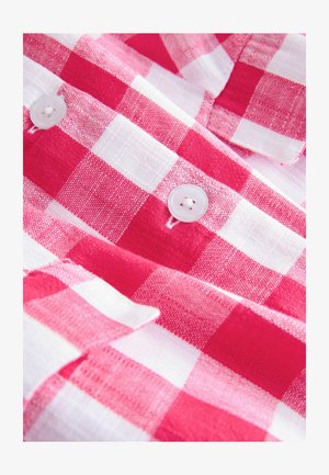 Tissu à carreaux rouges et blancs avec deux boutons blancs cousus dessus, montrant la texture détaillée et les coutures.