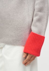 Γκρι πλεκτό πουλόβερ με ανάγλυφη υφή και μονόχρωμη φωτεινή κόκκινη μανσέτα. Ο λεπτός σχεδιασμός διαθέτει κανονική εφαρμογή και απαλό ύφασμα.