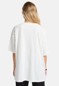 White oversized t-shirt made of cotton. Short sleeves, round neck, smooth texture. No visible patterns or accents. Simple design.