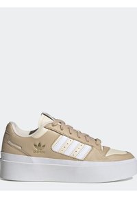 Beige ja valge Adidas spordijalats paksu valge tallaga, valged triibud külgedel, beežid paelad ja kullavärvi Adidas logo kontsapooles.