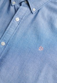 Camicia azzurra chiaro in morbido cotone. Presenta un colletto classico, bottoni bianchi e un piccolo logo ricamato sul petto.