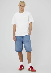 T-shirt en coton blanche avec un petit motif de citron, associée à un short en denim bleu clair et des baskets rouges avec des accents blancs.