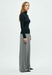 Tumši zils garām piedurknēm mākslā turtlenecks krekls kopā ar gaiši pelēku platā kāju biksēm. Gluda, cieša auduma ar minimāliem detaļām plūstošā silueta.