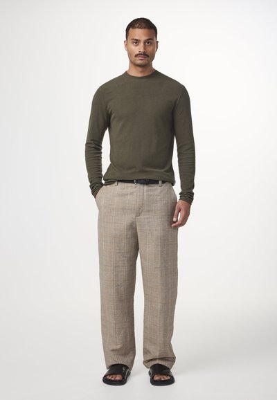 Camicia a maniche lunghe verde oliva, pantaloni a quadri chiari con tonalità beige e grigie, cintura nera e sandali neri. Design semplice e dritto.