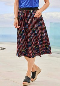 Jupe noire et rouge à motifs avec des rayures horizontales, taille élastique et design fluide, associée à des sandales à talons compensés noires.