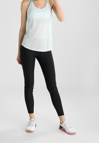 Canotta sportiva azzurro chiaro con spalline sottili abbinata a leggings neri e scarpe da ginnastica bianche con dettagli rosa. Tessuto liscio in tutta la superficie.