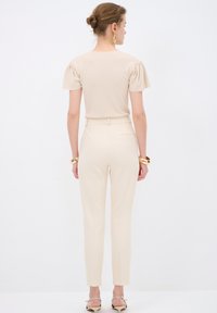 Beige, fitted top with short puff sleeves, paired with tailored beige trousers. Smooth texture, minimal design, and subtle back detail.