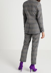 Costume à carreaux gris avec une veste cintrée et un pantalon fuselé, doté d'une fente à l'arrière et de six boutons noirs. Associé à des bottines violettes.