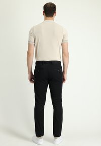 Polo beige de manga corta con un acabado texturizado y un sutil cuello de canalé, combinado con pantalones negros que cuentan con bolsillos traseros y un corte slim.