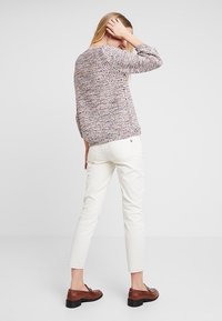 Suéter de punto con patrones y mangas largas, jeans de color claro y mocasines marrones. El suéter presenta un diseño texturizado y multicolor.