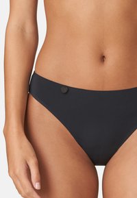 Schwarzer Bikiniunterteil, nahtloses Design, niedrig geschnitten, glatte Textur, mit einem runden schwarzen Akzentknopf an der linken Hüfte.