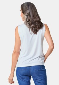 Lichtgrijze mouwloze top met een gladde textuur, met een ronde halslijn. Gecombineerd met donkerblauwe jeans, gezien van de achterkant.