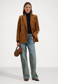 Bruin corduroy dubbelzijdig jasje over een zwarte turtleneck, gecombineerd met lichtblauwe wijde jeans en een bruine handtas.