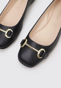 Bailarinas negras hechas de cuero sintético suave, con punta cuadrada, herrajes en tono dorado y un detalle de hebilla decorativa.
