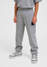 Grijze joggingbroek met een elastische tailleband, voorzien van een klein zwart stoffen label. Gecombineerd met grijze en witte sneakers. Zachte textuur.