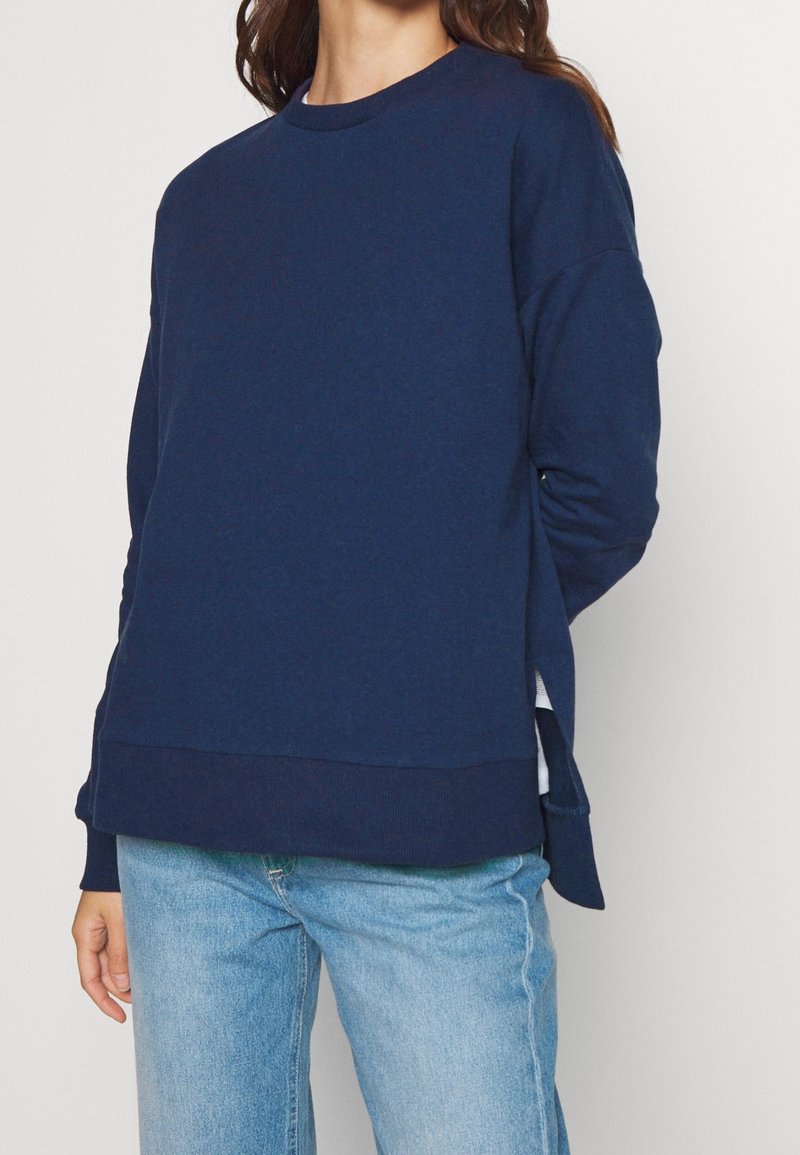 Sweatshirt blu navy realizzato in tessuto morbido, con collo a giro, maniche lunghe e aperture laterali all'orlo per facilitare i movimenti.