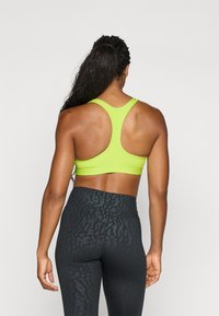 Sostén deportivo de un brillante color verde lima con un diseño de espalda racer, combinado con leggings negros de cintura alta que presentan una sutil textura de estampado animal.