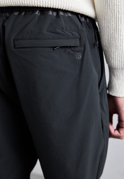 Mustat housut, jotka on valmistettu kevyestä kankaasta ja joissa on teksturoitu pinta. Housuissa on joustava vyötärö, takatasku ja logo-aksentti.