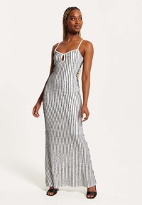 Maxi dress in a black and white striped pattern with a keyhole front, thin spaghetti straps, and a fitted silhouette. Smooth fabric texture.