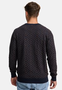 Pull marin à motif et design en losanges, avec des poignets et un ourlet côtelés, en tissu texturé, et un col rond ; porté de manière décontractée sur un denim clair.