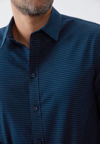 Camisa de botones azul marino con pequeños patrones de cuadrados blancos, un cuello bien definido y una textura suave, que cuenta con un cierre frontal de botones.