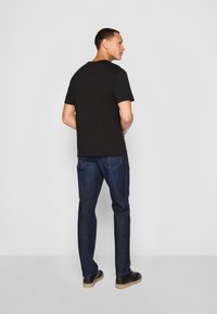 Camiseta negra de manga corta, material de algodón, corte relajado. Combinada con unos jeans de mezclilla azul oscuro, pierna recta, detalles de costura sutiles y zapatos negros.