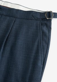 Tailored navy trousers made of textured fabric, featuring pleats, side pockets, and a metal buckle on the waistband.