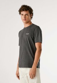 Grijze t-shirt met korte mouwen, gemaakt van zachte stof, met een ronde hals en een klein wit logo op de borst. Minimalistisch ontwerp.