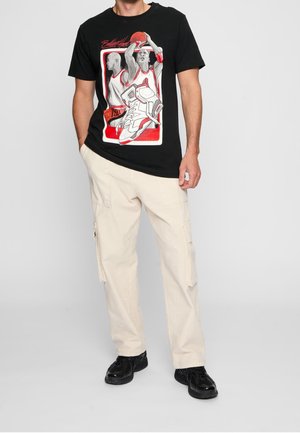 Black t-shirt with basketball player graphic in red and white. Features short sleeves and a round neckline. Casual fit complemented by beige cargo pants.