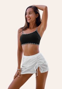 Černý cropped top s stříbrnými detaily, v kombinaci s bílou síťovanou sukní na šňůrku, která předvádí texturovanou látku a nastavitelné detaily.