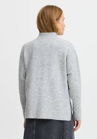 Grauer, weicher, gestrickter Pullover mit hohem Kragen, überschnittenen Schultern und lässiger Passform, der eine strukturierte Oberfläche und seitliche Schlitze zeigt.