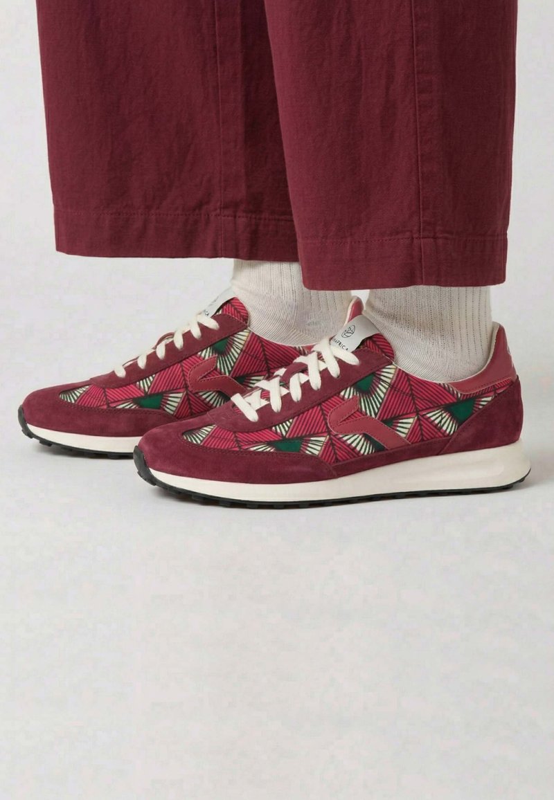Paire de baskets rouges à motifs géométriques avec des lacets blancs, portées avec des chaussettes blanches et un pantalon rouge large.